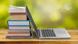 a laptop computer with books on top of it on a wooden table