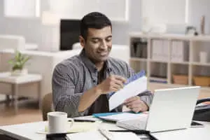 a man is sitting at a desk and looking at his laptop
