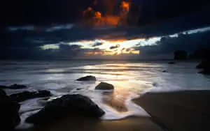 a dark sky and waves at sunset