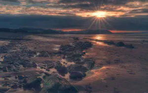 a beach with rocks and a sun setting behind it